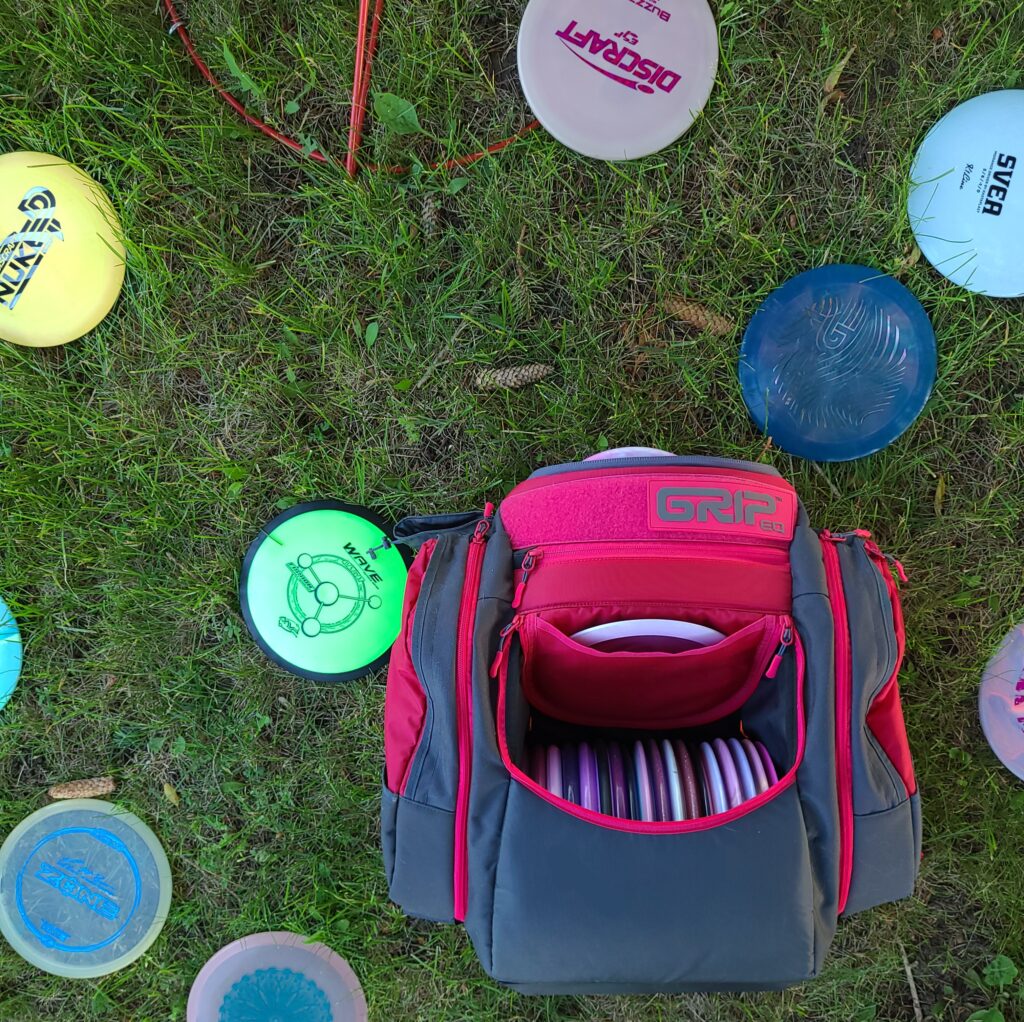 A shot from above of a pink GRIPeq AX5 bag as it sits on the ground full of discs. Several other discs are scattered around the ground next to it.