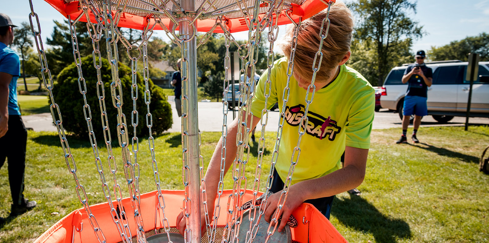A young disc golfer reaching into a portable disc golf basket to retrieve his disc at a players clinic event.