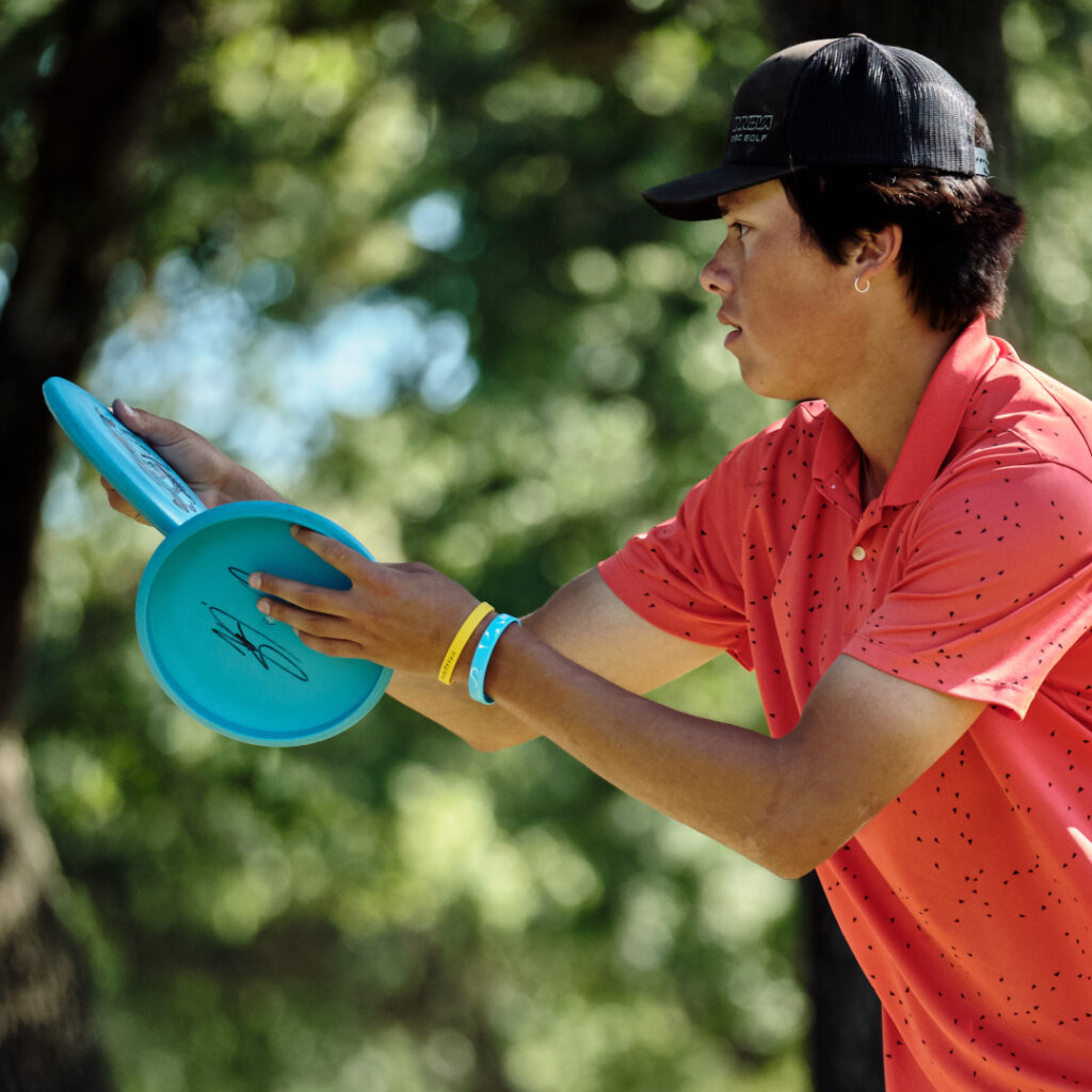 A profile view of Anthony Barela as he holds two discs in his hands and prepares to putt.