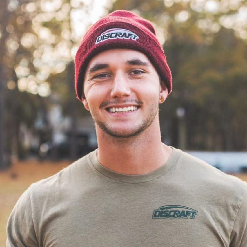 A shot of Austin Turner smiling at the camera, wearing a Discraft beanie.