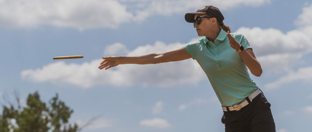 A side view of Holly Finley throwing a disc. The disc is mid-flight after just leaving her hand.