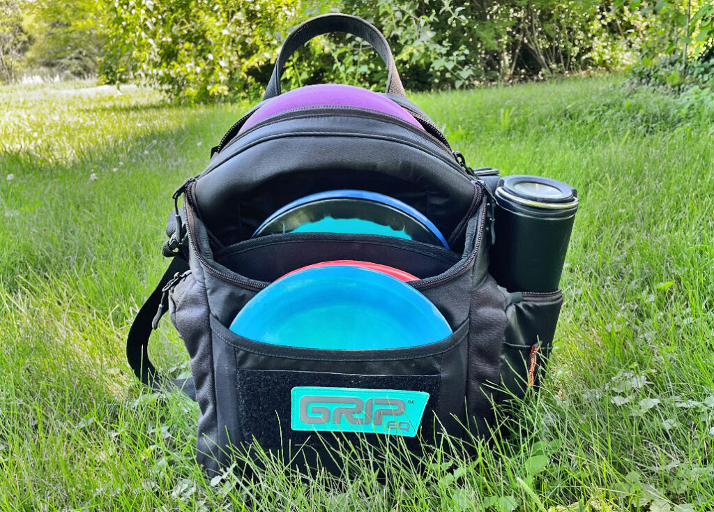 A GRIPeq G2 bag, loaded with discs and a water bottle, sits in the grass.
