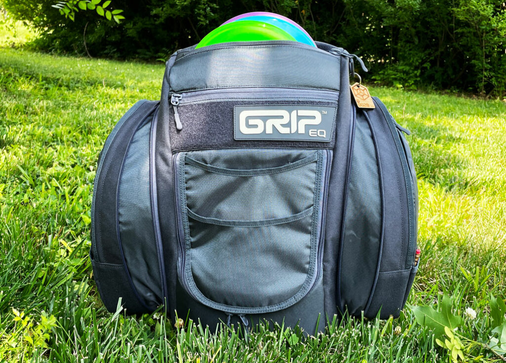 A GRIPeq bag sits in the grass with its expandable side pockets open and full.