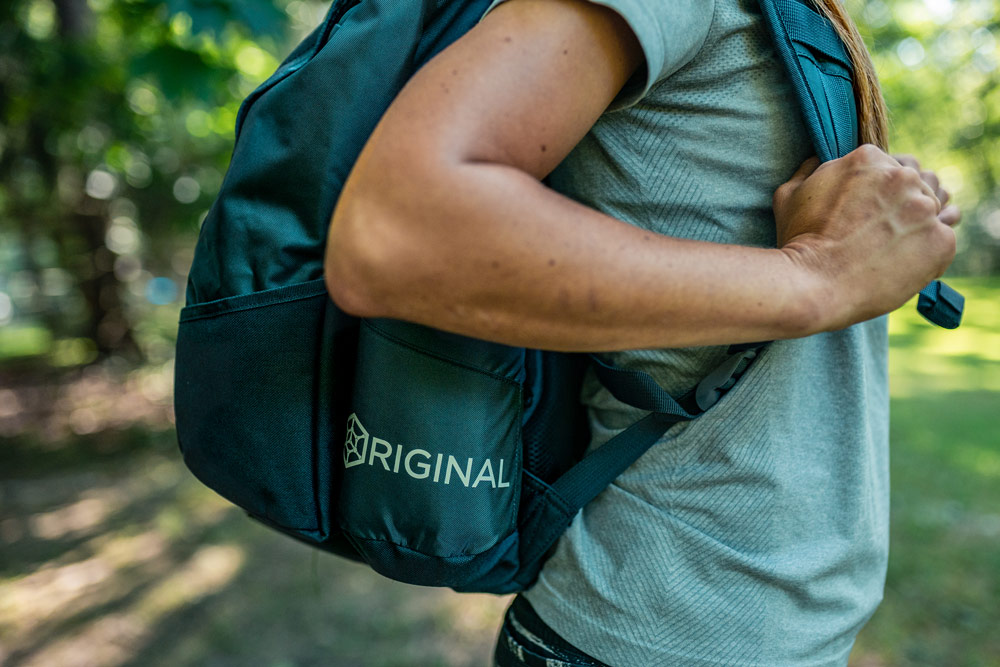 A side closeup view of a GRIPeq bag on someones back, highlighting the word Original on the water bottle pocket.