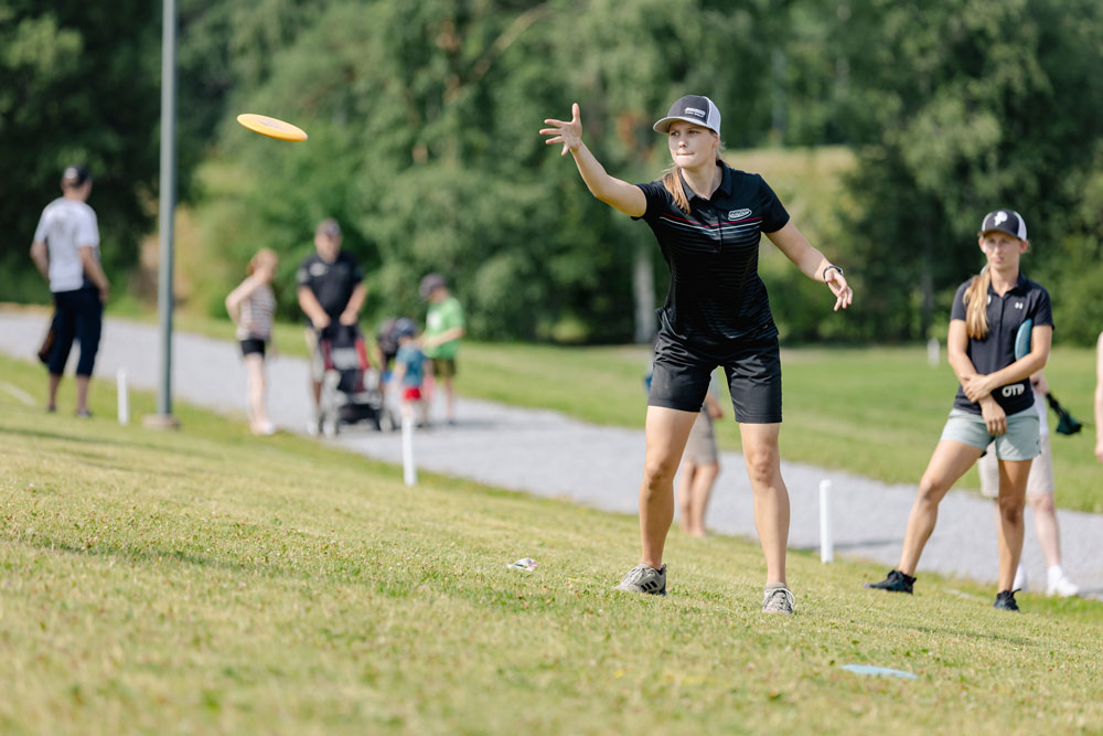 Henna Blomroos, Team GRIPeq member, throws a putt. The disc is shown mid flight and there are spectators in the background.