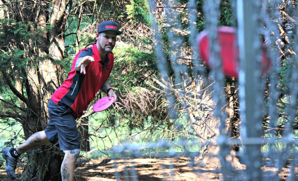 Patrick Brown making a disc golf putt with the basket in the foreground.