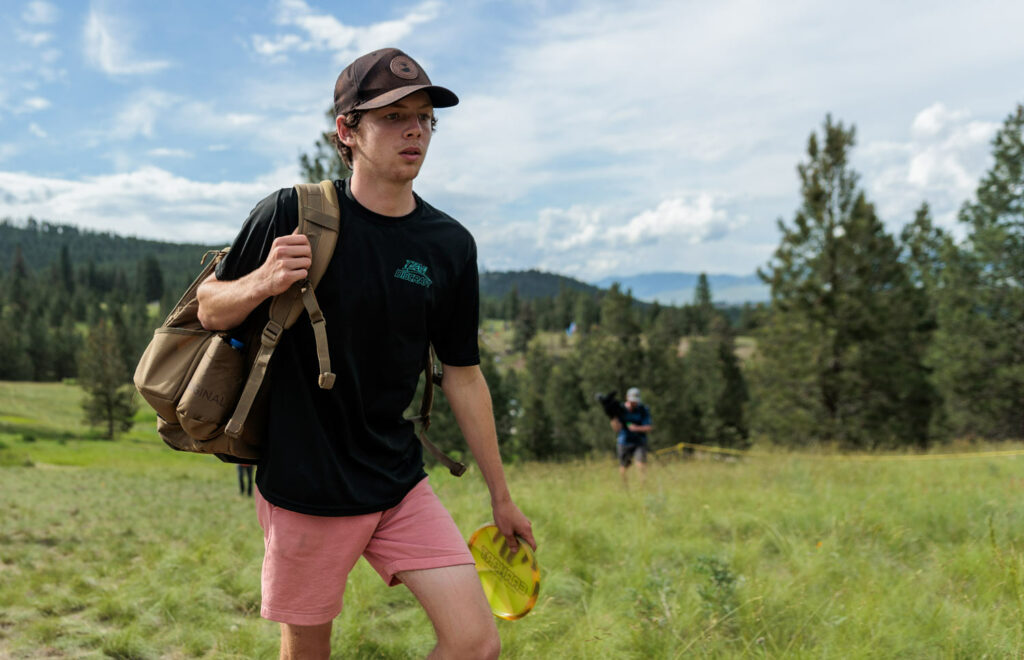 Team GRIPeq member, Evan Scott, walks the disc golf course with his GRIPeq bag over his shoulder at the Zoo City Open. A mountain range is in the background.