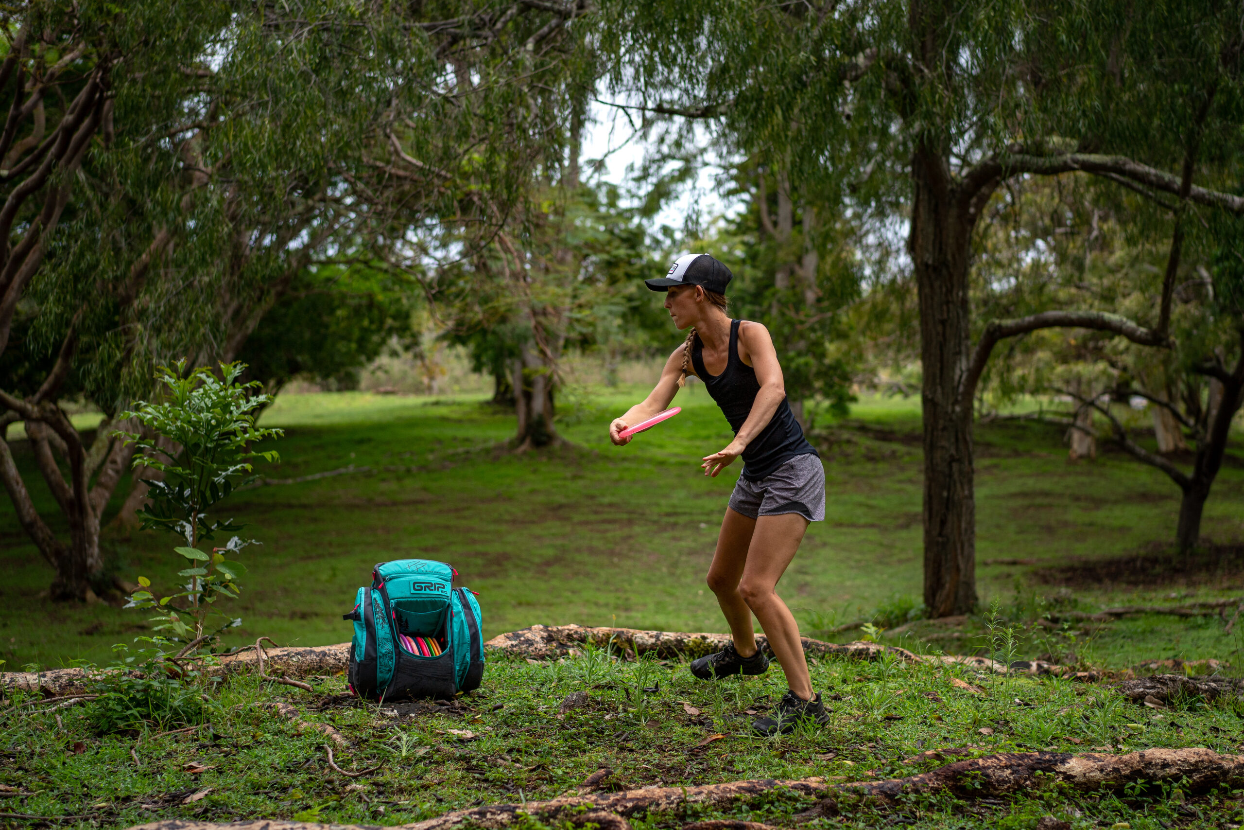 A rear view shot of Team GRIPeq member, Paige Pierce, throwing a disc in Hawaii as her signature series BX3 bag sits next to her on the ground.