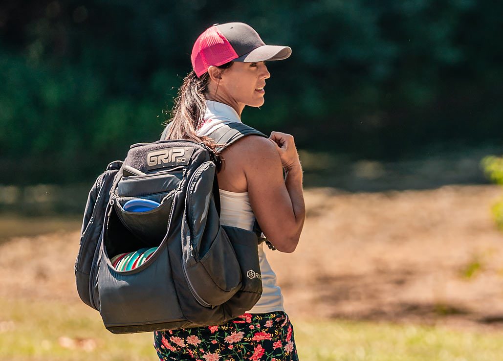 Jennifer Allen walks on the course with a gray GRIPeq AX5 bag on her back. She's looking back over her shoulder with her right hand grasping the strap.