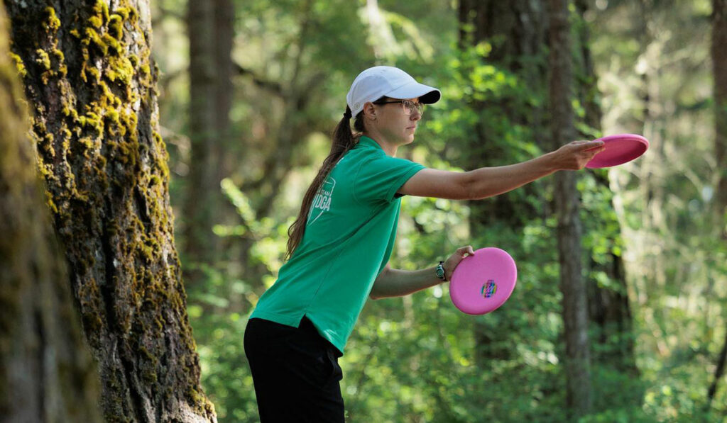 Side profile view of Team GRIPeq member Ali Smith as she lines up a putt with a disc in each hand.