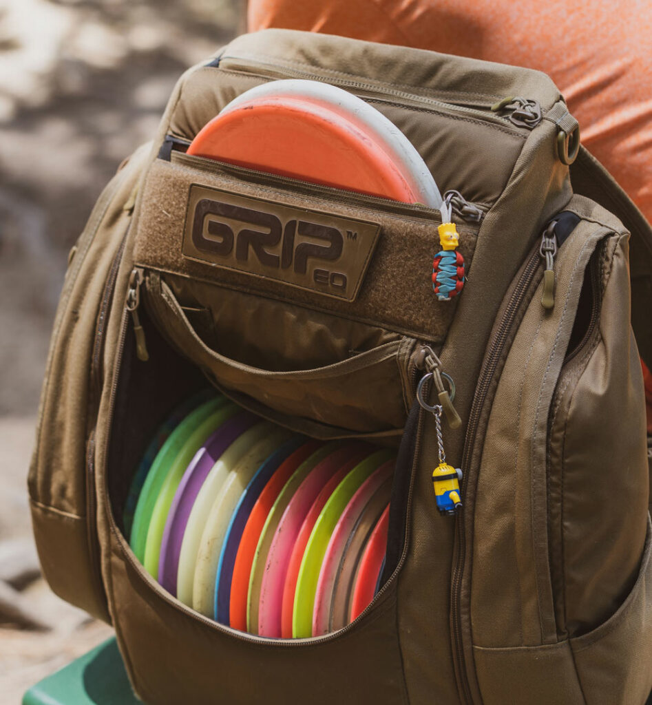 A sand GRIPeq BX3 bag sits next to a player, loaded with discs.