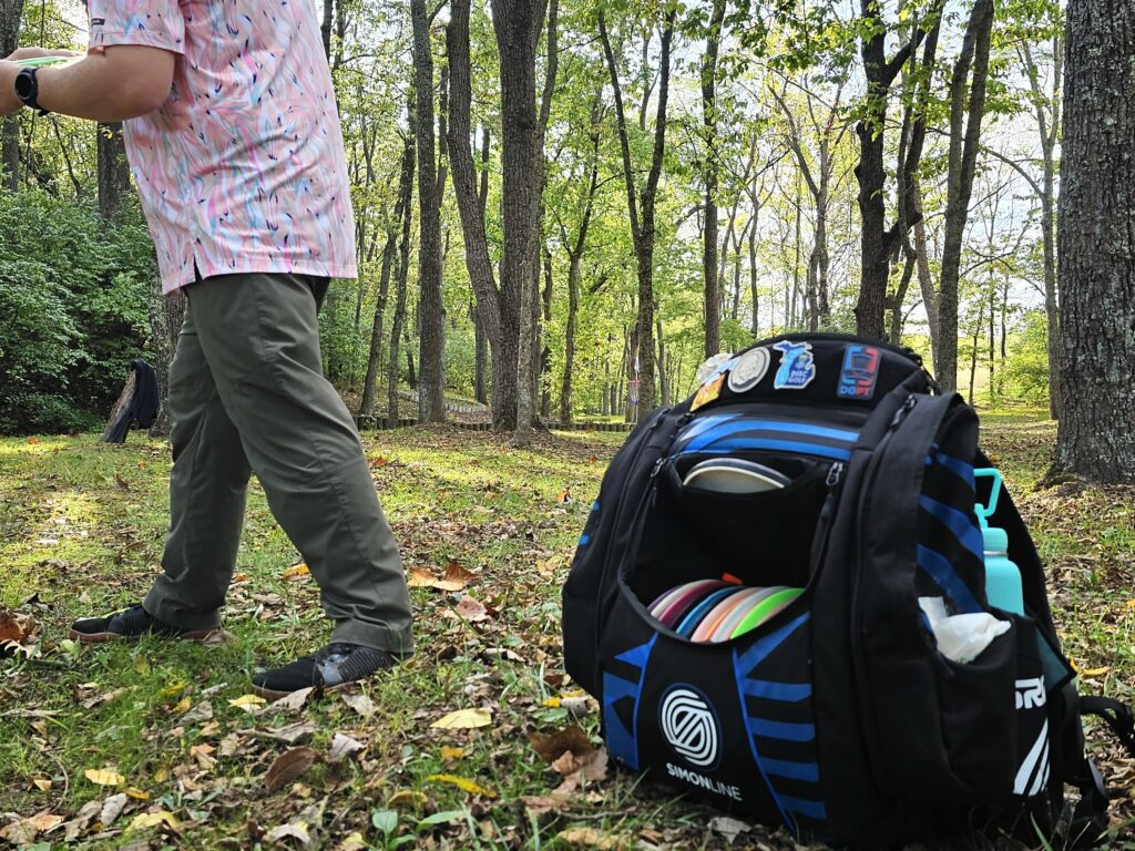 A disc golfer prepares to throw his disc with a GRIPeq Simon Line bag sitting on the ground next to him.