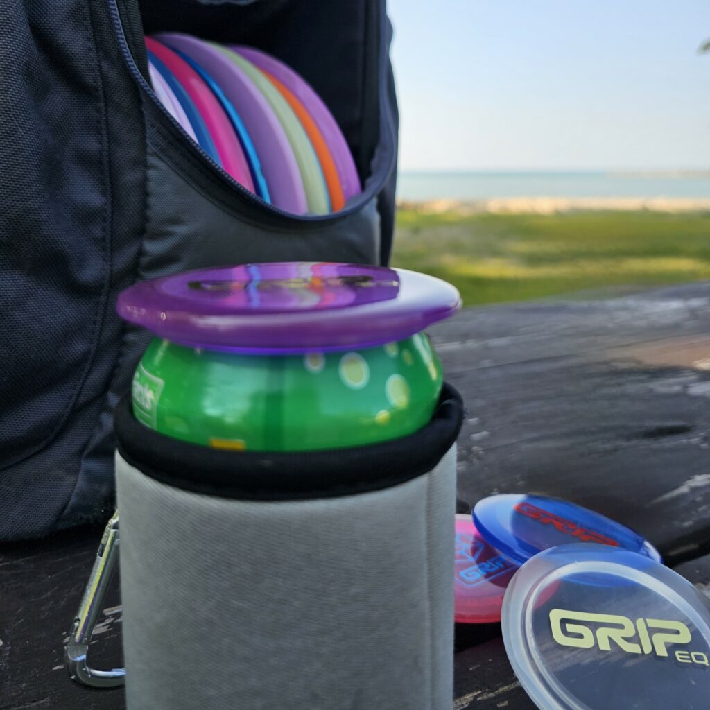 A 12oz can with a GRIPeq Can Topper on top. A few can toppers are seen in the background near a Gray GRIPeq CS2 bag.
