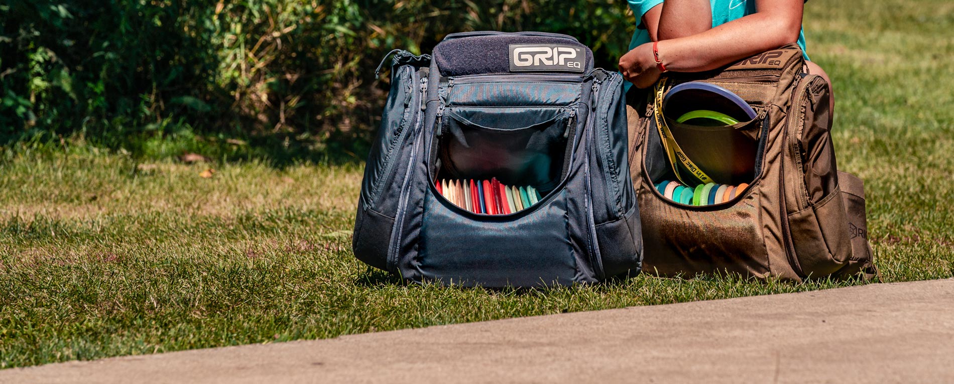 Two GRIPeq disc golf bags sit on the ground.
