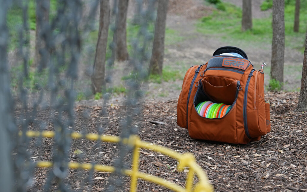 An orange GRIPeq bag sits on the ground with a basket in the foreground.