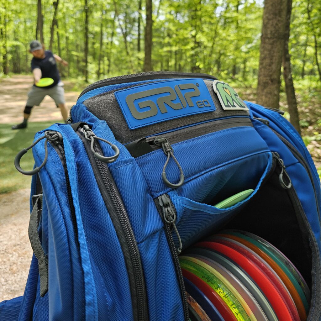 A blue GRIPeq AX6 bag with a player driving a disc in the background.