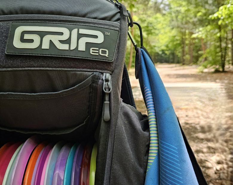 One GRIPeq bag featuring a D Ring and a towel attached to the ring with a carabiner clip. There's a disc golf fairway in the background.